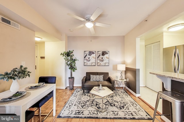 living room with baseboards, visible vents, and a ceiling fan