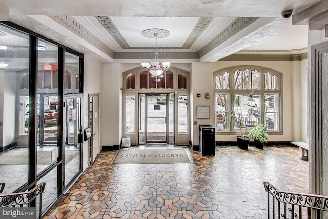 foyer entrance with a tray ceiling, crown molding, baseboards, and an inviting chandelier