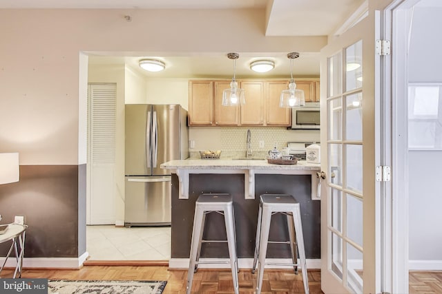 kitchen with a breakfast bar area, stainless steel appliances, light countertops, light brown cabinets, and a sink