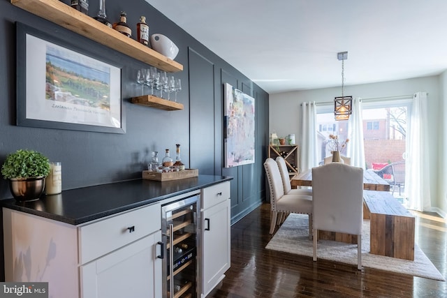 bar featuring dark wood-style floors, wine cooler, hanging light fixtures, and a bar