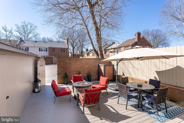 wooden terrace featuring outdoor dining space, fence, a fire pit, and a residential view