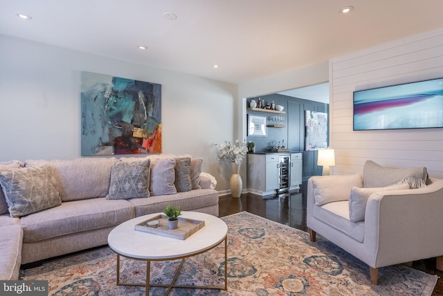 living area featuring dark wood-style flooring, a dry bar, recessed lighting, wood walls, and beverage cooler