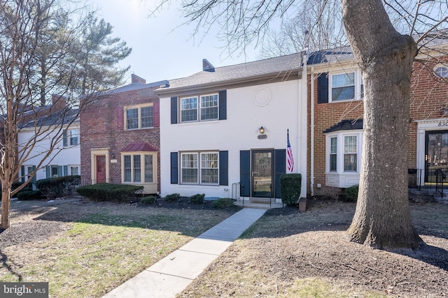 townhome / multi-family property featuring brick siding, a chimney, and a front lawn