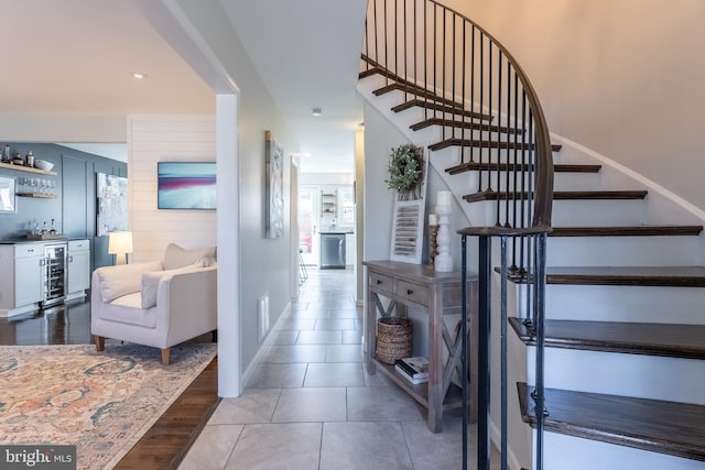 stairs with visible vents, a bar, tile patterned flooring, beverage cooler, and baseboards