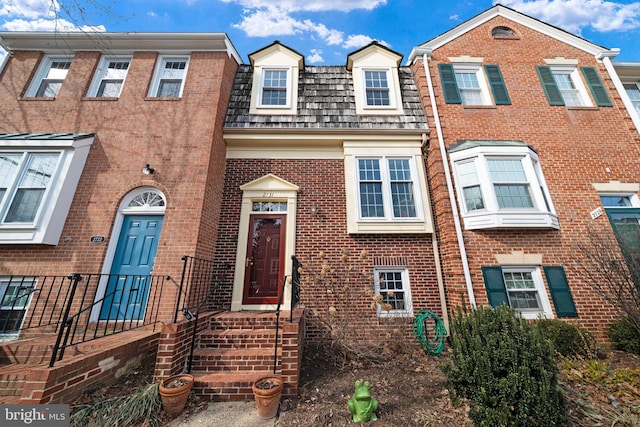 view of property featuring brick siding and mansard roof