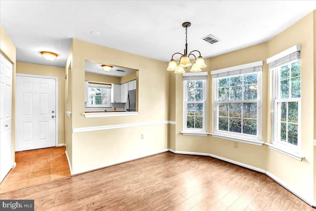 unfurnished dining area with a chandelier, baseboards, visible vents, and light wood-style floors