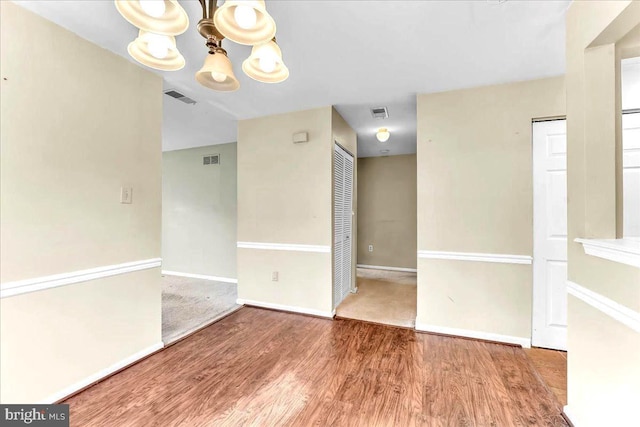 spare room featuring an inviting chandelier, visible vents, baseboards, and wood finished floors