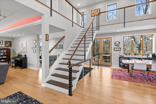 stairway featuring visible vents, a towering ceiling, baseboards, and wood finished floors