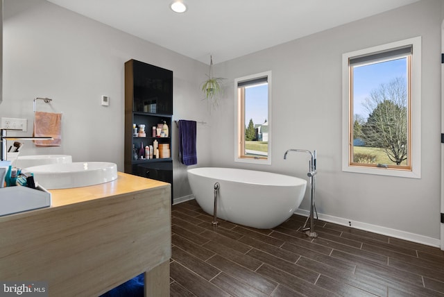 full bath featuring baseboards, vanity, a freestanding bath, and wood tiled floor