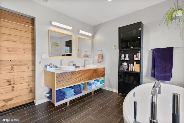 full bath with double vanity, a freestanding tub, wood finish floors, and a sink