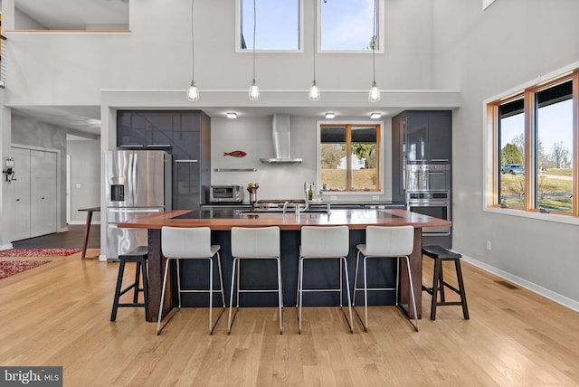 kitchen with a breakfast bar area, wooden counters, light wood-type flooring, wall chimney range hood, and stainless steel fridge