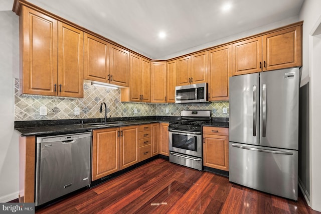 kitchen with sink, appliances with stainless steel finishes, dark hardwood / wood-style floors, dark stone counters, and backsplash