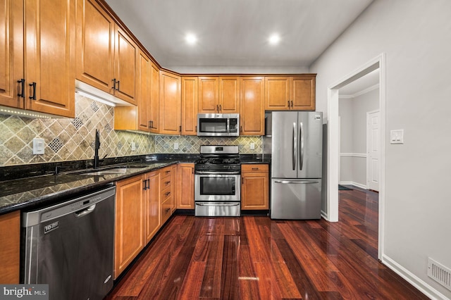 kitchen with appliances with stainless steel finishes, tasteful backsplash, sink, dark stone counters, and dark wood-type flooring