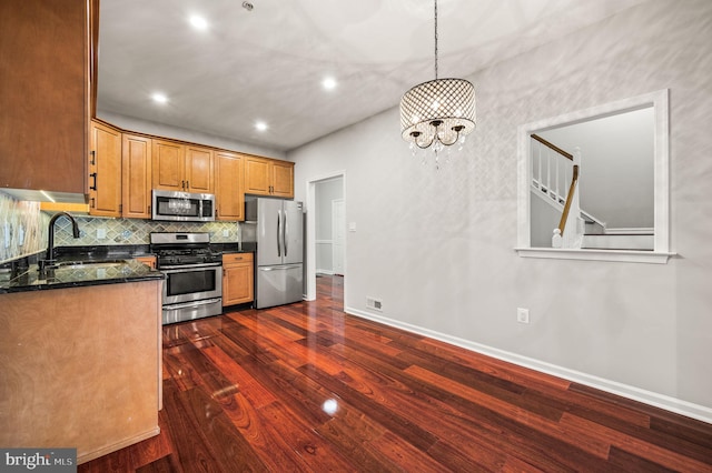 kitchen featuring appliances with stainless steel finishes, dark hardwood / wood-style floors, decorative light fixtures, sink, and dark stone counters