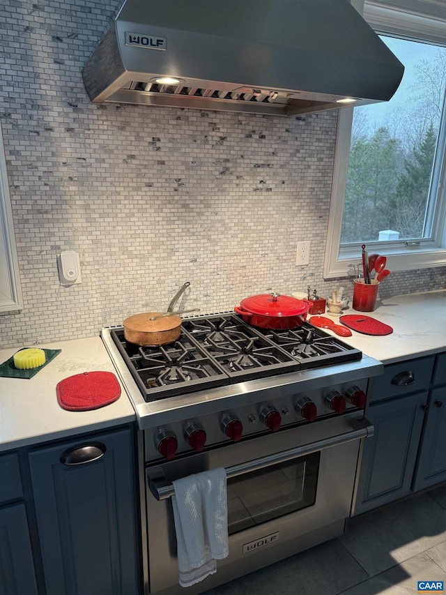 kitchen featuring blue cabinetry, custom exhaust hood, tasteful backsplash, light tile patterned floors, and high end stove