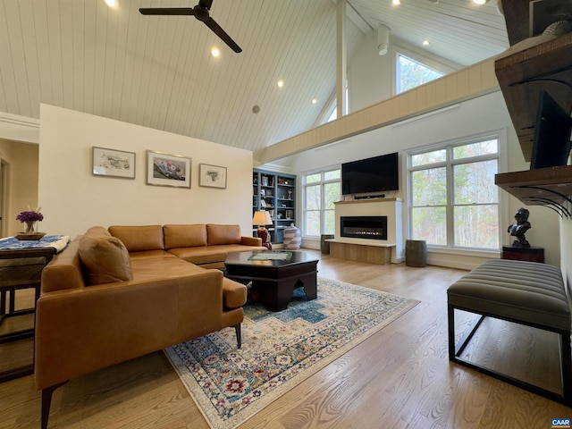 living room with built in shelves, high vaulted ceiling, light hardwood / wood-style flooring, ceiling fan, and beam ceiling