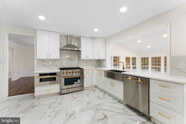 kitchen featuring a peninsula, a sink, white cabinets, appliances with stainless steel finishes, and wall chimney exhaust hood