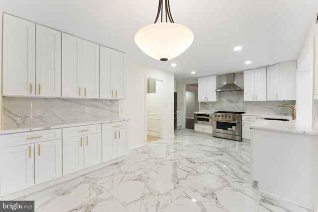 kitchen featuring pendant lighting, marble finish floor, stainless steel appliances, white cabinetry, and wall chimney range hood