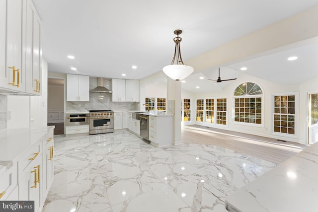 kitchen featuring pendant lighting, appliances with stainless steel finishes, open floor plan, white cabinetry, and wall chimney range hood