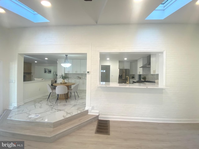 kitchen with high quality fridge, a skylight, visible vents, light countertops, and wall chimney range hood