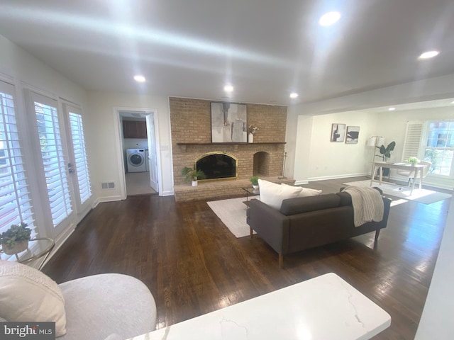 living room featuring washer / dryer, a brick fireplace, baseboards, and dark wood-type flooring