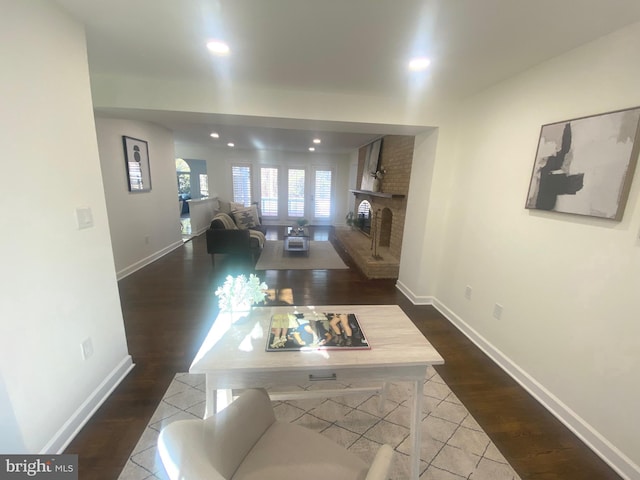 living area with dark wood-type flooring, a brick fireplace, and baseboards