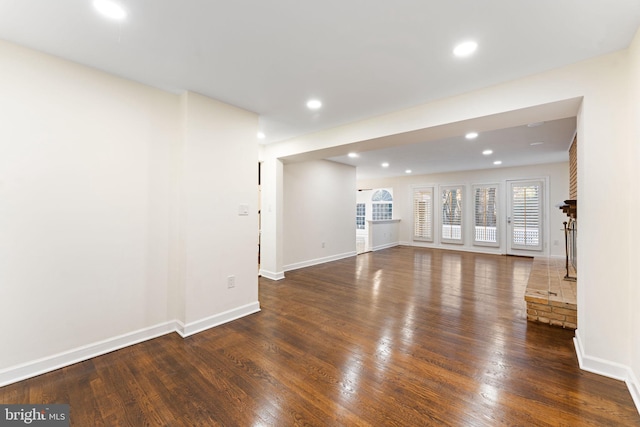 unfurnished living room featuring dark wood-type flooring, recessed lighting, a brick fireplace, and baseboards