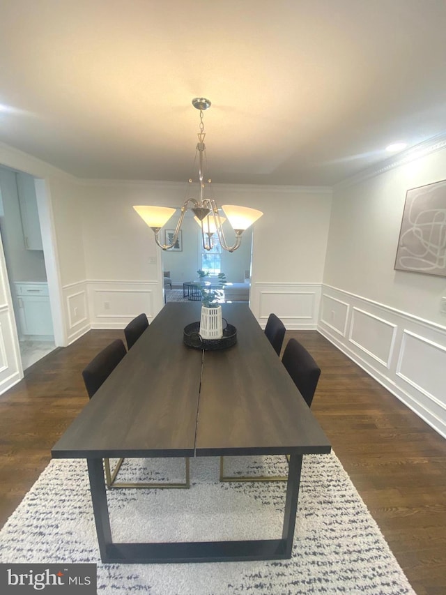 dining space featuring dark wood-style floors, a decorative wall, crown molding, and an inviting chandelier