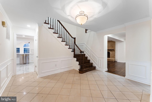 foyer with light tile patterned floors, stairway, a decorative wall, and crown molding