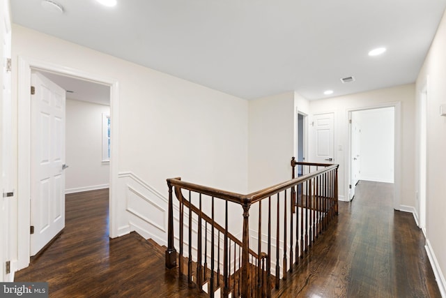 hall with dark wood-style floors, visible vents, and an upstairs landing