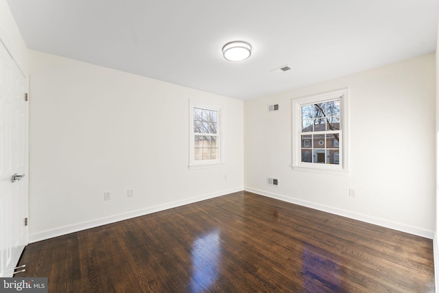 empty room featuring dark wood-style flooring, visible vents, and baseboards