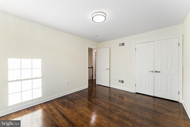 unfurnished bedroom with dark wood-style floors, baseboards, visible vents, and a closet