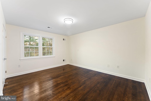 empty room featuring dark wood finished floors, visible vents, and baseboards