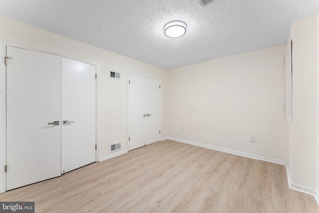 unfurnished bedroom with a textured ceiling, light wood-style flooring, visible vents, and baseboards