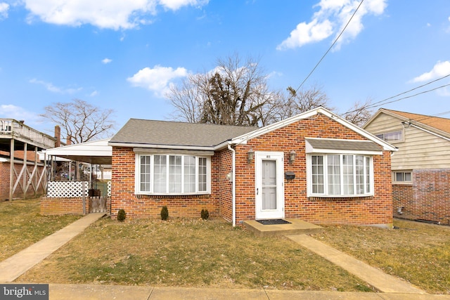 bungalow-style house with a shingled roof, a front lawn, an attached carport, and brick siding