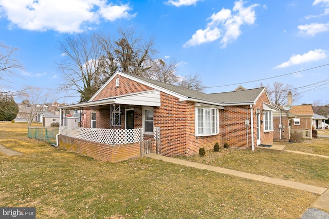 view of front of house with covered porch, fence, a front lawn, and brick siding