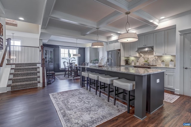 kitchen with a kitchen island with sink, hanging light fixtures, and light stone counters