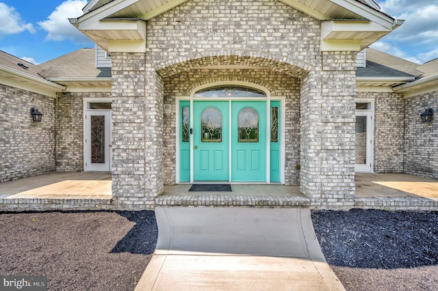 entrance to property featuring brick siding and roof with shingles