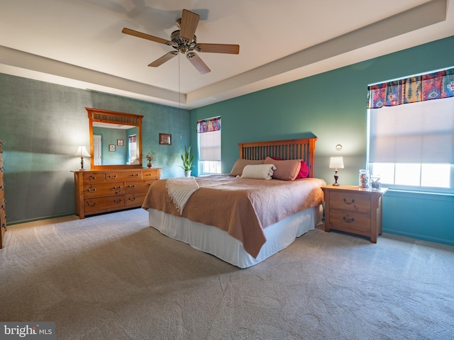 bedroom with a tray ceiling, ceiling fan, carpet flooring, and multiple windows