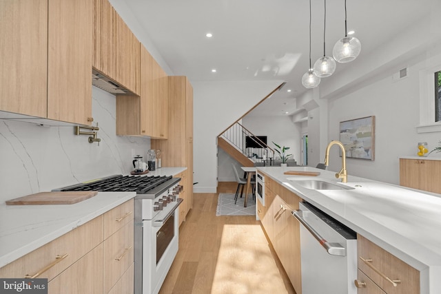 kitchen with light brown cabinetry, sink, stainless steel dishwasher, light hardwood / wood-style floors, and gas range