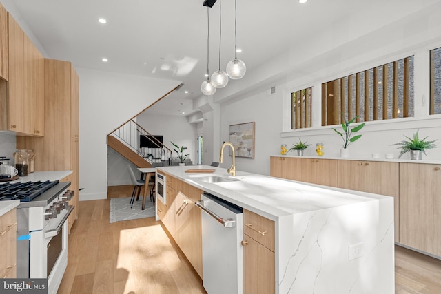 kitchen featuring appliances with stainless steel finishes, pendant lighting, sink, light stone countertops, and a center island with sink