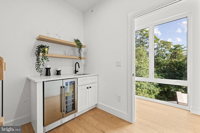 bar with beverage cooler, sink, light hardwood / wood-style flooring, and white cabinets