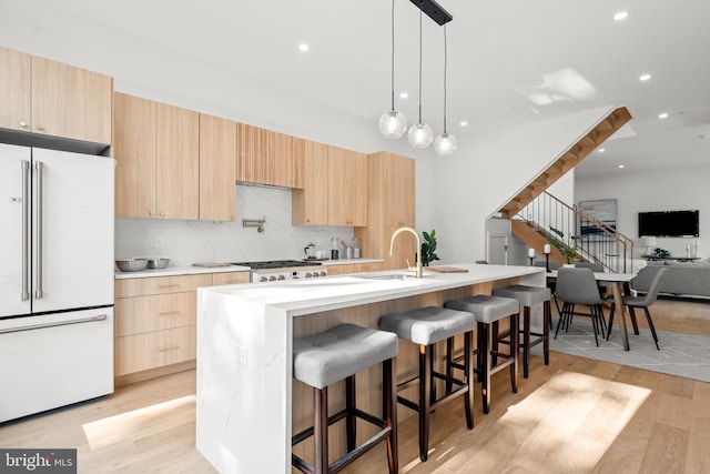 kitchen with sink, high end fridge, hanging light fixtures, a center island with sink, and light brown cabinets