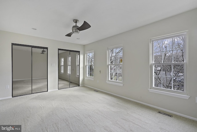 unfurnished bedroom featuring carpet flooring, two closets, visible vents, and baseboards