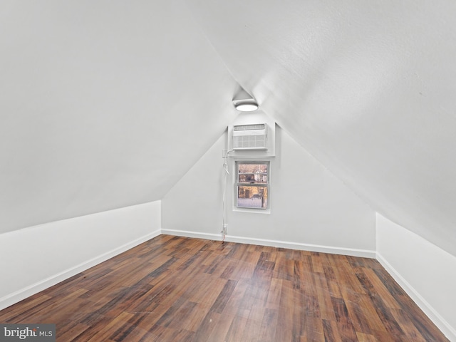 additional living space featuring vaulted ceiling, dark wood-type flooring, and a wall unit AC