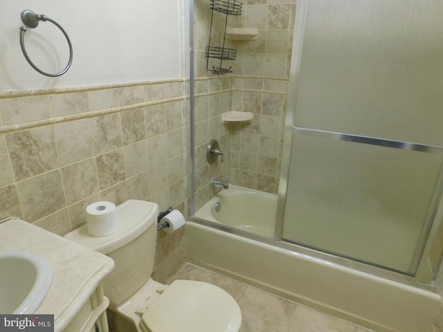 full bathroom with tile walls, shower / bath combination with glass door, vanity, and toilet