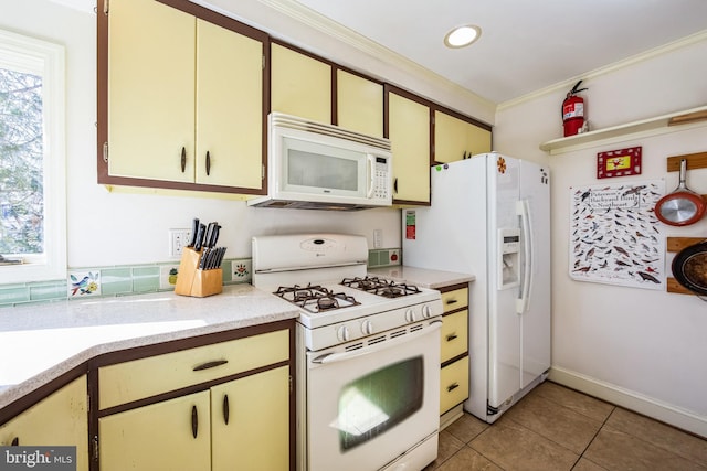 kitchen featuring light tile patterned floors, light countertops, cream cabinets, ornamental molding, and white appliances