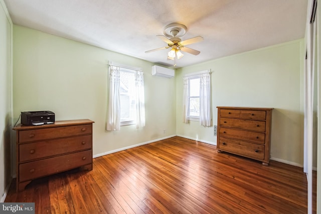 bedroom with an AC wall unit, wood-type flooring, a ceiling fan, and baseboards