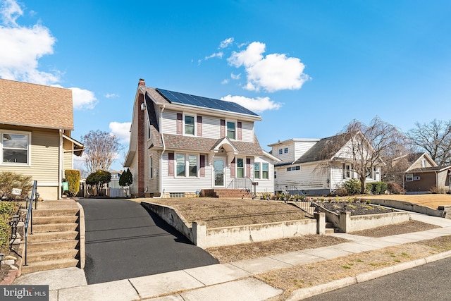 view of front of property featuring driveway, a chimney, fence, and roof mounted solar panels