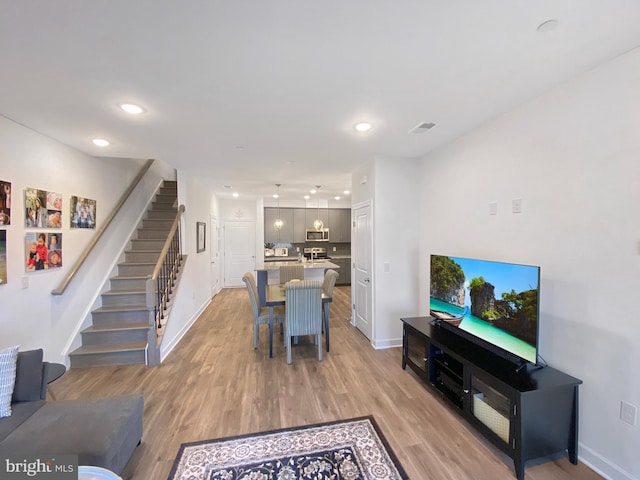 living room featuring light wood-type flooring, baseboards, recessed lighting, and stairs